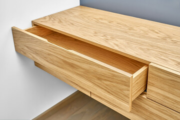 Stylish floating cabinet of natural wood with opened empty drawer near white wall in contemporary...