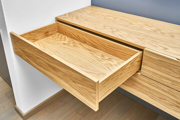 Stylish floating cabinet of natural wood with opened empty drawer near white wall in contemporary apartment interior design closeup