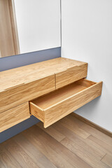 Stylish floating cabinet of natural wood with opened empty drawer near white wall in contemporary apartment interior design closeup