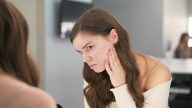 Girl with the problem of acne during puberty, looks at herself in the mirror. Close-up