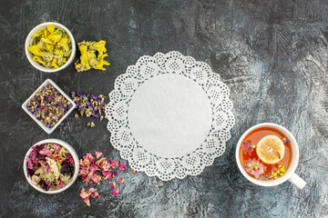 Obraz na płótnie Canvas a piece of lace with herbal tea with lemon and flowers with bowls of dry flowers on grey ground