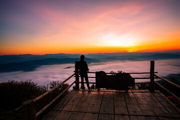 Fototapeta premium The silhouette of a woman sitting in front of the sunrise on the hill with the sea of ​​clouds In the north of Thailand, Doi Samer Dao, Nan Province