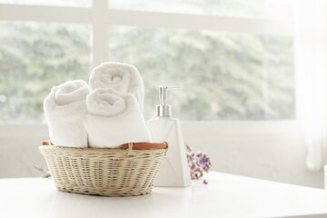 Fototapeta na wymiar Towel placed on basket, white table top, bottle of liquid soap, spa set for bathing in the bathroom, copy space, bathroom window.