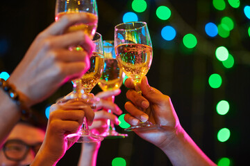 Cropped image of young people toasting with glasses of champagne when celebrating New Year in night...