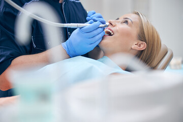 Naklejka premium Dentist treating young attractive woman with machine