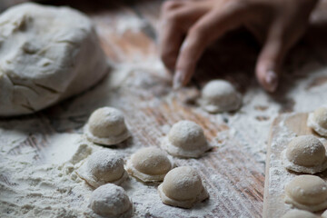 
Cooking dumplings. Raw dumplings lie on a wooden board. Nearby lies flour, rolling pin and dough against a background of wood.
