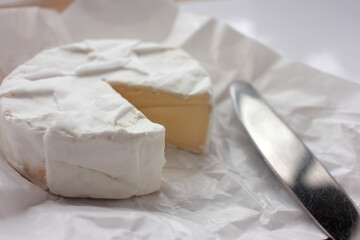 Camembert cheese on white packaging paper. Top view. Close up of white cheese