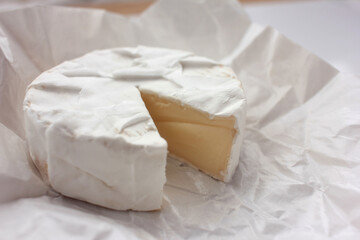 Fototapeta na wymiar Camembert cheese on white packaging paper. Top view. Close up of white cheese