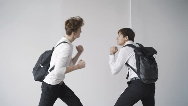 Side view of angry teenagers arguing and fighting in school corridor. Two Caucasian students pushing and hitting. Adolescent learners fight indoors. Anger and adolescence concept.