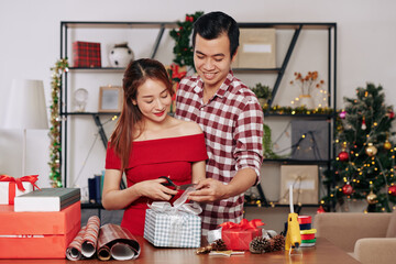 Young Asian couple in love wrapping and decorating Christmas presents for holiday season together