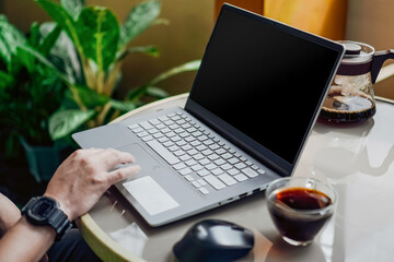 Man working on a laptop with blank screen in a fresh and clean outdoor environment with a cup of coffee/tea.	