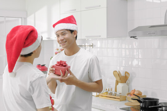Young asian LGBT gay couple celebrating christmas and happy new year party by exchange gift each other in the kitchen on holiday. Selective focus. - Powered by Adobe
