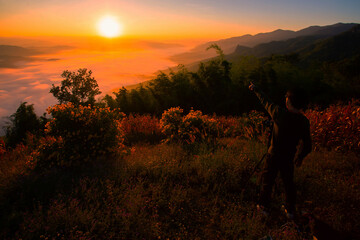 A photographer taking pictures of the sunrise And beautiful fog on the top of a tall mountain in Thailand
