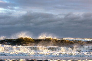 Rough surf under dark ominous storm clouds, with spray coming off large waves breaking. 