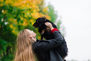 Young attractive woman holding her dachshund dog in her arms outdoors in sunrise in park at autumn