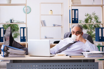 Old male employee drinking coffee in the office