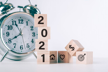 wooden cubes with the New year 2021 and goal, health, finance, and Home icon. New year target plan with wood blocks cubes on wooden and clock table