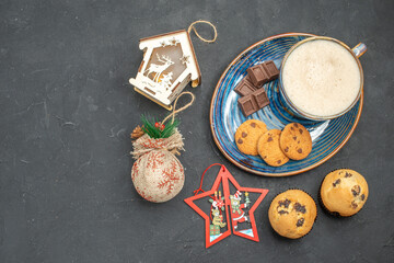 Obraz na płótnie Canvas Top view of delicious breakfast with a cup of milk various biscuits cakes and chocolate bars next to new year decorations on dark background