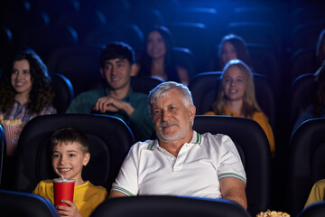 Grandfather with grandson enjoying cartoon in cinema hall.