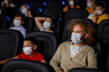 Multiracial family wearing face masks in movie theater.