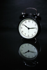 Black alarm clock on a mirror surface.