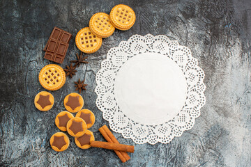 overhead shot of a piece of white lace with cookies and cinnamon and chocolate on grey background