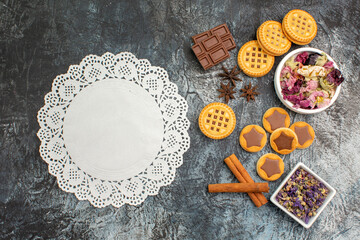 a piece of lace with different sort of cookies and bowls of dry flowers on grey ground