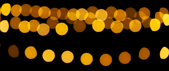 Gold lights garland in defocus on a black background. Yellow circles bokeh.