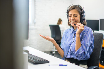 Friendly beautiful customer service agent woman chatting with client using hands-free headset at office.