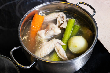 chicken wings soup is cooked in steel stewpot close up on stove at home kitchen isolated on white background