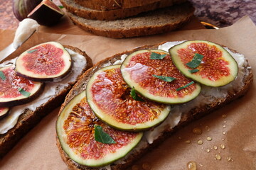 Figs. Sandwiches with figs, cheese, arugula, honey and nuts on wooden board over textured purple backdrop. Homemade. Everyday autumn kitchen. Vertical.