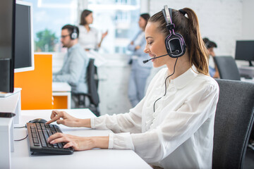 Attractive female helpline worker using computer in call centre office. - obrazy, fototapety, plakaty