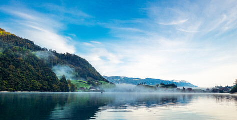 one morning at a lake in the European alps where the clouds are sun the valley and the landscape reflecting on the smooth water with a blue sky with clouds 