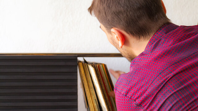 Primer plano de un hombre adulto cauc&aacute;sico buscando en su biblioteca de discos algun disco de vinilo para oir mientras se relaja en un ambiente blanco y bien iluminado