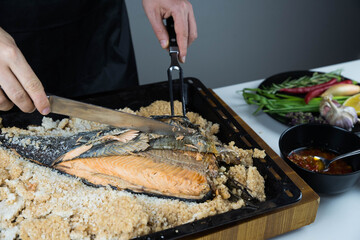 Chief cook is breaking salt and carving fish baked in salt crust. Seafood cooking. Salmon or...