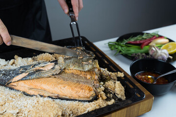 Chief cook is breaking salt and carving fish baked in salt crust. Seafood cooking. Salmon or...