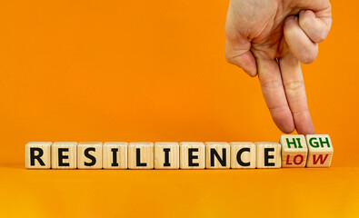 High or low resilience symbol. Male hand flips wooden cubes and changes words 'resilience low' to 'resilience high'. Beautiful orange background, copy space. Business and high resilience concept.