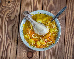 Chicken soup in a deep bowl, chicken drumstick and spoon in a deep bowl