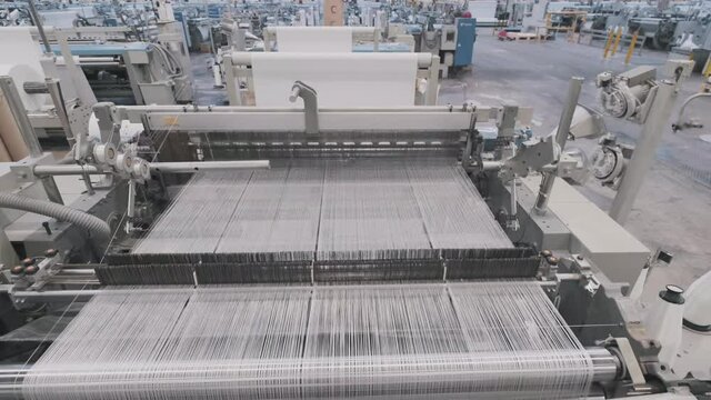 glass fiber production at the factory, macro fiberglass stretches through holes at plant. closeup large loom weaves white synthetic fiber