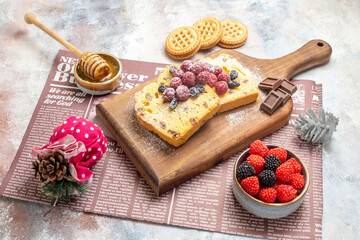 bottom view raisin cake slices with raspberries on cutting board bowl with raspberry candies biscuits honeycomp stick in honey bowl xmas toy and a newspaper on marble ground