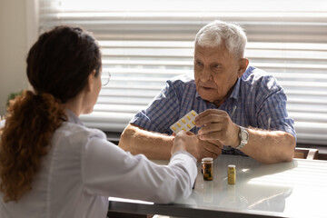 Woman GP or therapist give recommend pills or drugs to unhealthy mature male patient in clinic. Caring female doctor prescribe medicines to sick senior man client. Elderly healthcare concept.