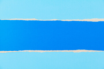 Torn piece of blue cardboard on blue paper background. Stripe of blue cardboard with copy space for text.