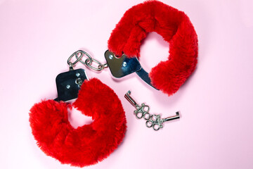 Red sexy fluffy handcuffs with keys on a pink background.