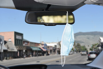 Closeup of a surgical or Covid-19 mask hanging from the rear view mirror of a car.