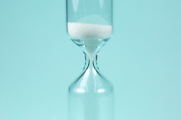 Sand clock on turquoise background. Hourglass as time passing concept. Close up photo.