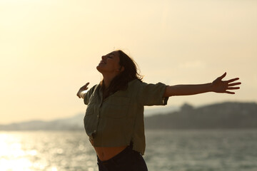 Silhouette of excited woman stretching arms on the beach