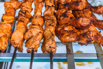 Closeup of skewed chicken legs tandoori slowly cooking over charcoal
