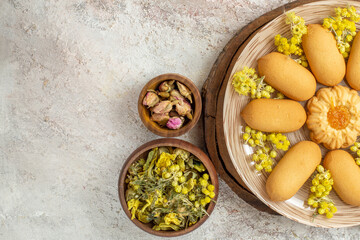 half-left view of a plate of cookies on wooden platter and bowls of dry flowers on marble background