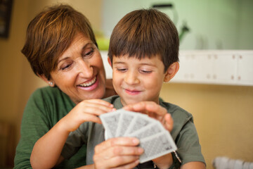 Adorable smiling couple of boy and his grandmother playing cards game.
