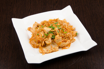chicken stew with fried onions and spices in white plate on wooden background